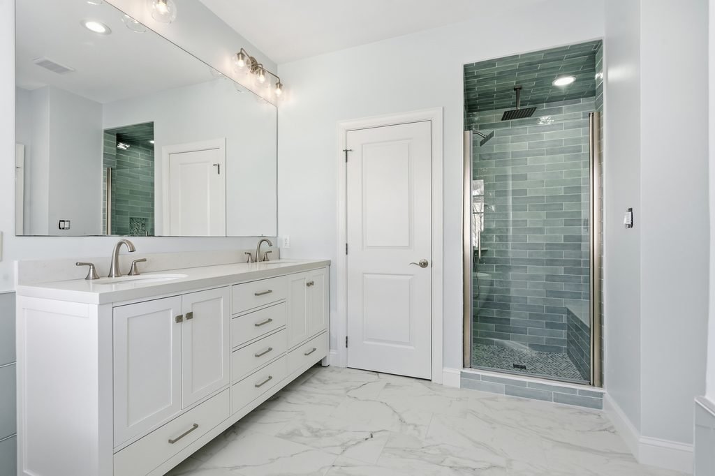 bathroom design with white vanity & a large wall mirror with coordinating lighting & shower