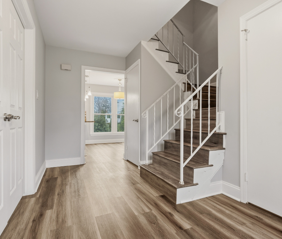 Modern home hallway with light brown hardwood flooring leading past a staircase.